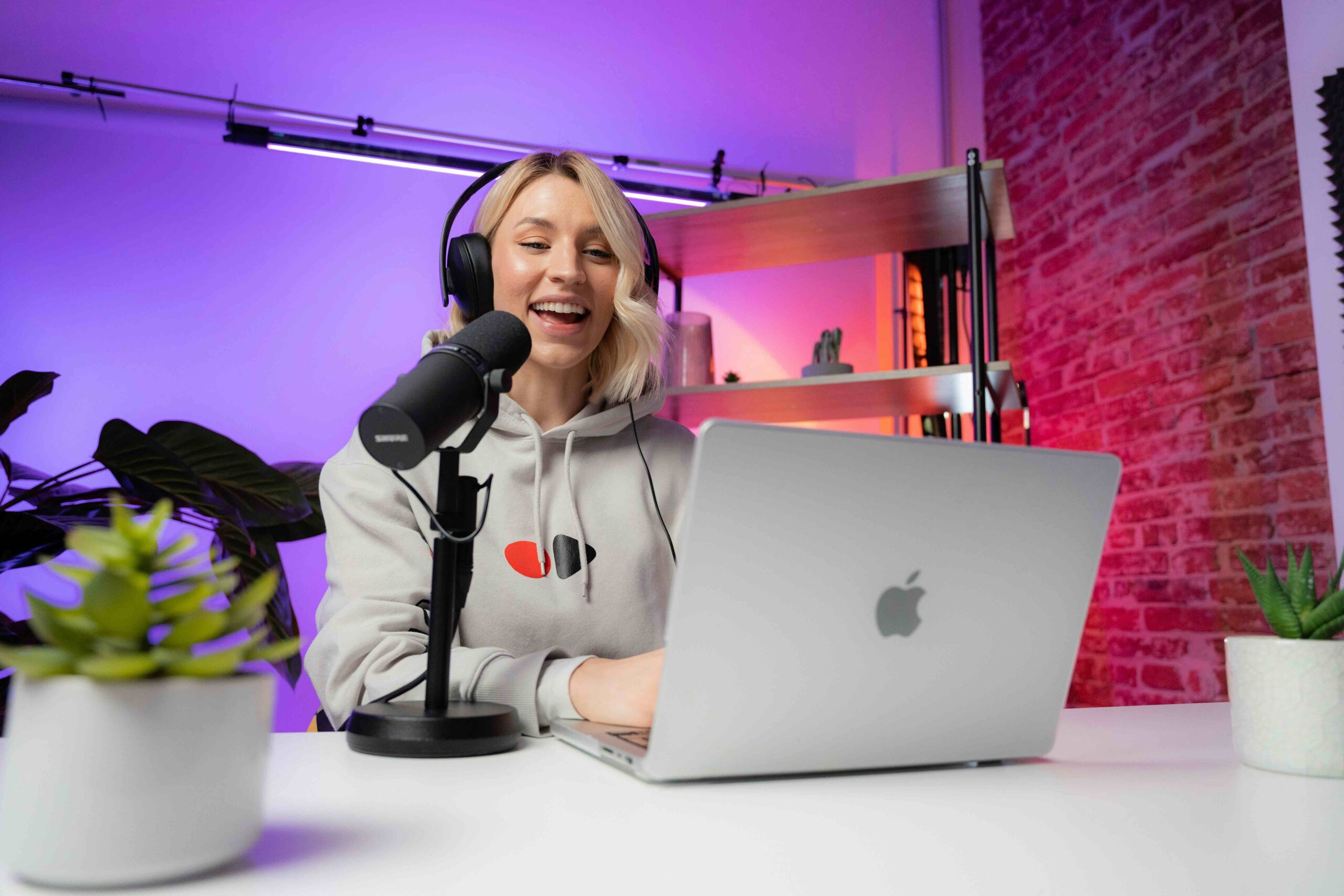 Blonde woman on her MacBook with a podcasting mic next to her and headphones on