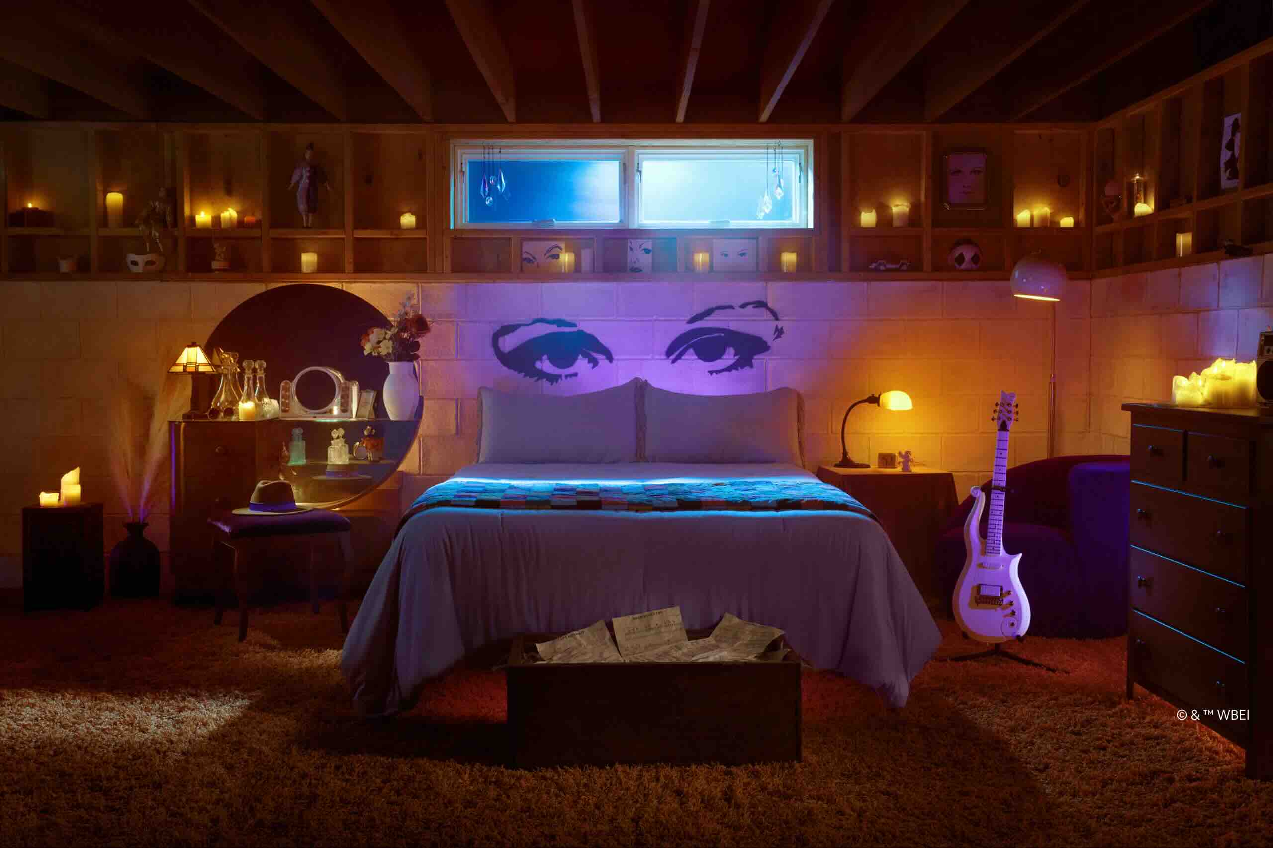 AirBnB's listing and image of Prince's Purple Rain house. Image shows inside the bedroom, with the bed visible and purple lights behind it. A guitar is on the right hand side and vases on the left.