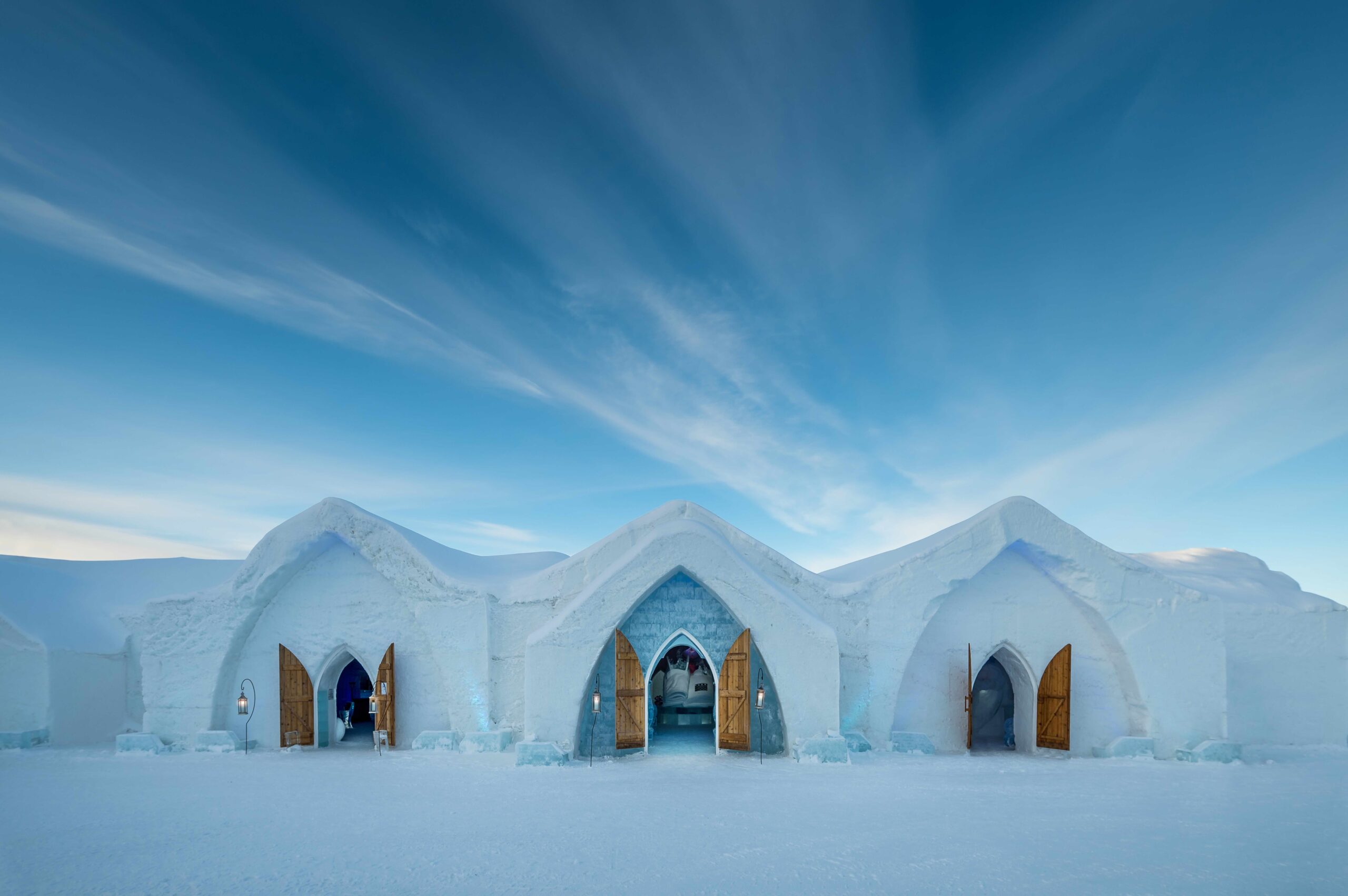 Blue skies with an ice restaurant in the forefront. It has three curved entrances, each with a door at the front.