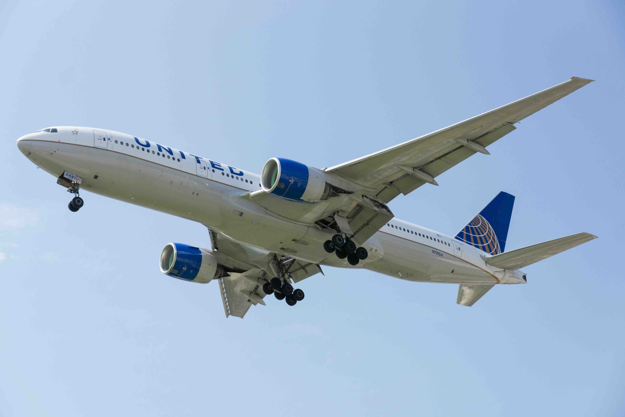 United Airlines plane in the air, can see the underside with the blue sky in the background.