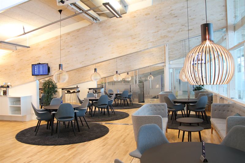 Airport lounge, neutral with sofas and chair inside and wooden floor.