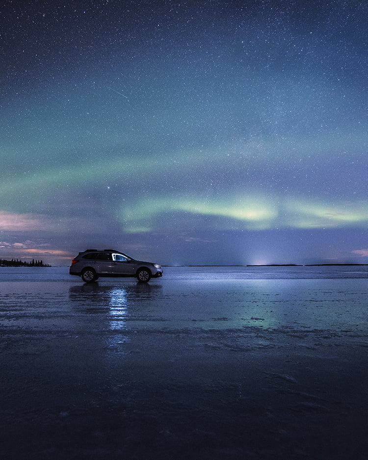 Northern lights visible in the dark sky, with a car parked underneath.
